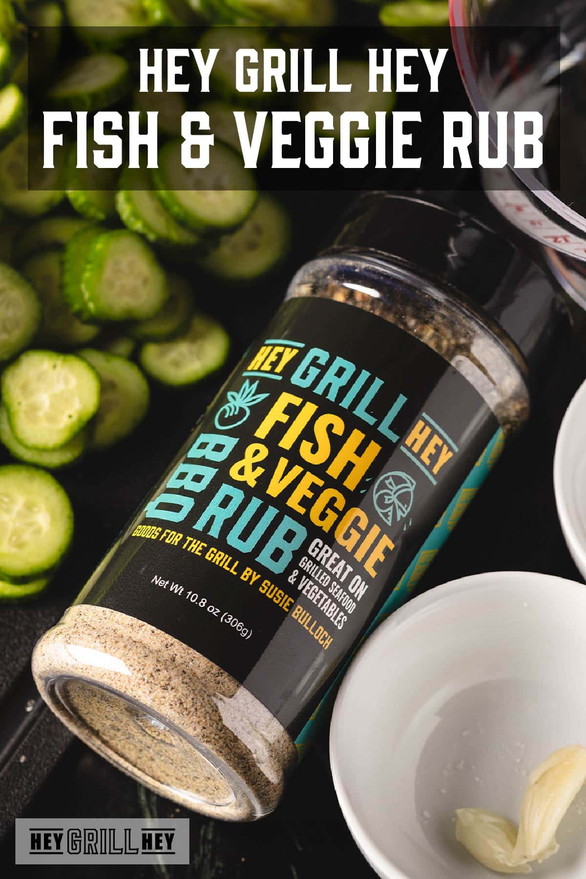 Jar of Fish & Veggie Rub next to pickle slices and white bowl of garlic. Text reads "Hey Grill Hey Fish & Veggie Rub."