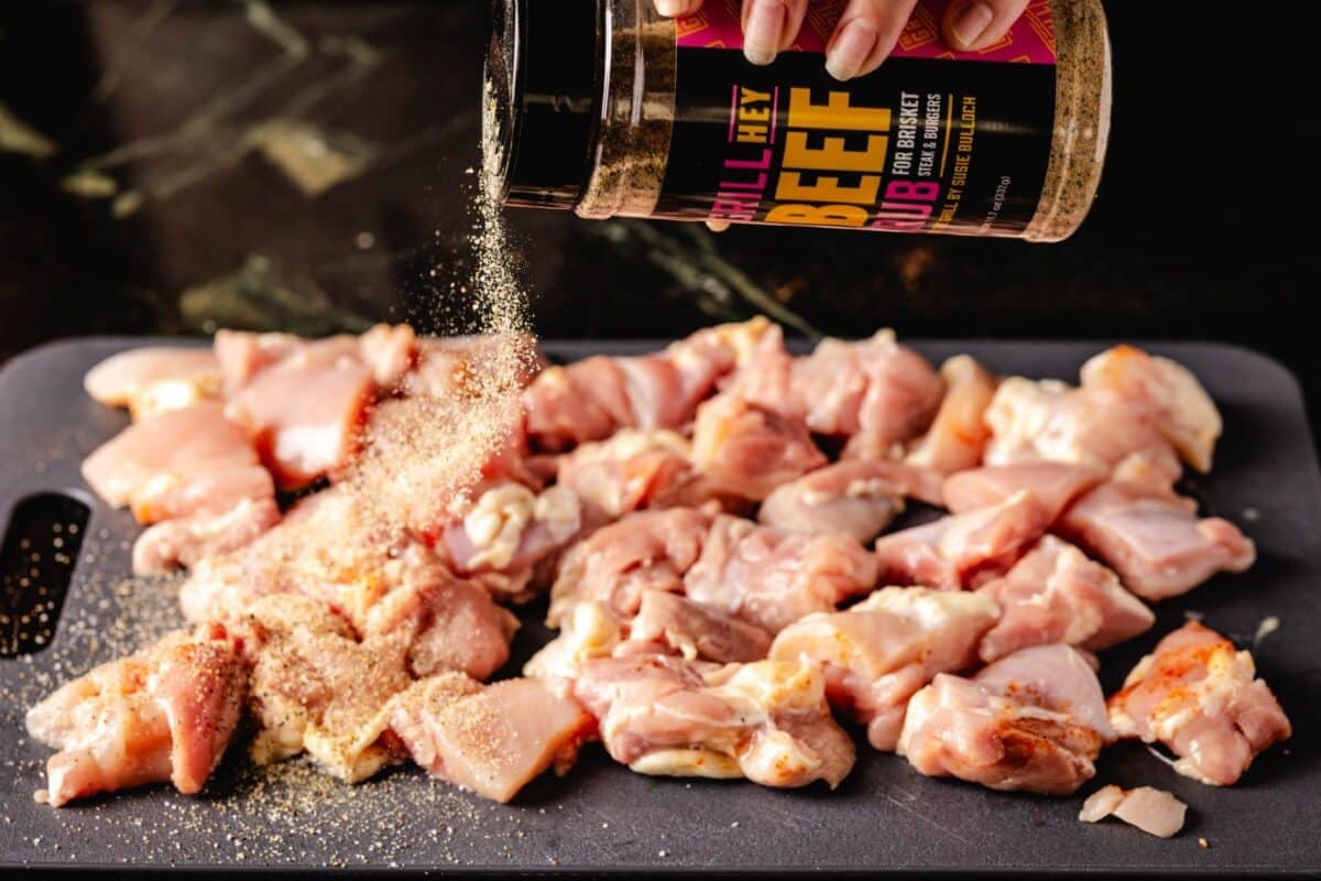 Chicken thighs on cutting board being seasoned with Beef Rub.