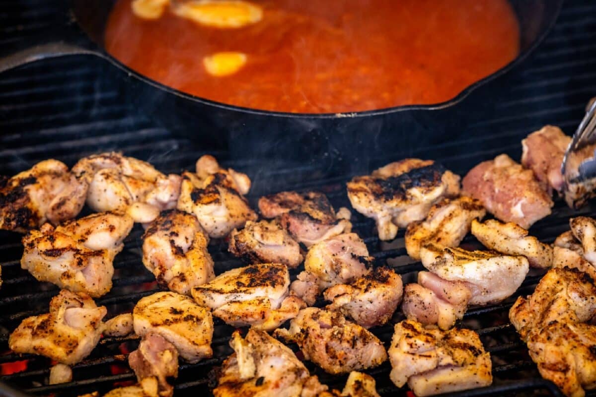 Grilled chicken thighs next to skillet of sauce.