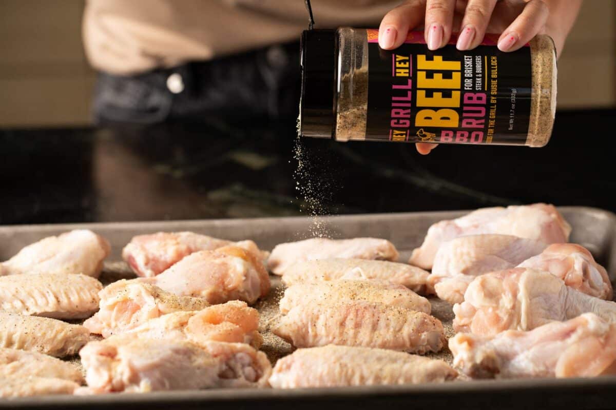 Raw chicken on baking sheet being seasoned with Beef Rub.