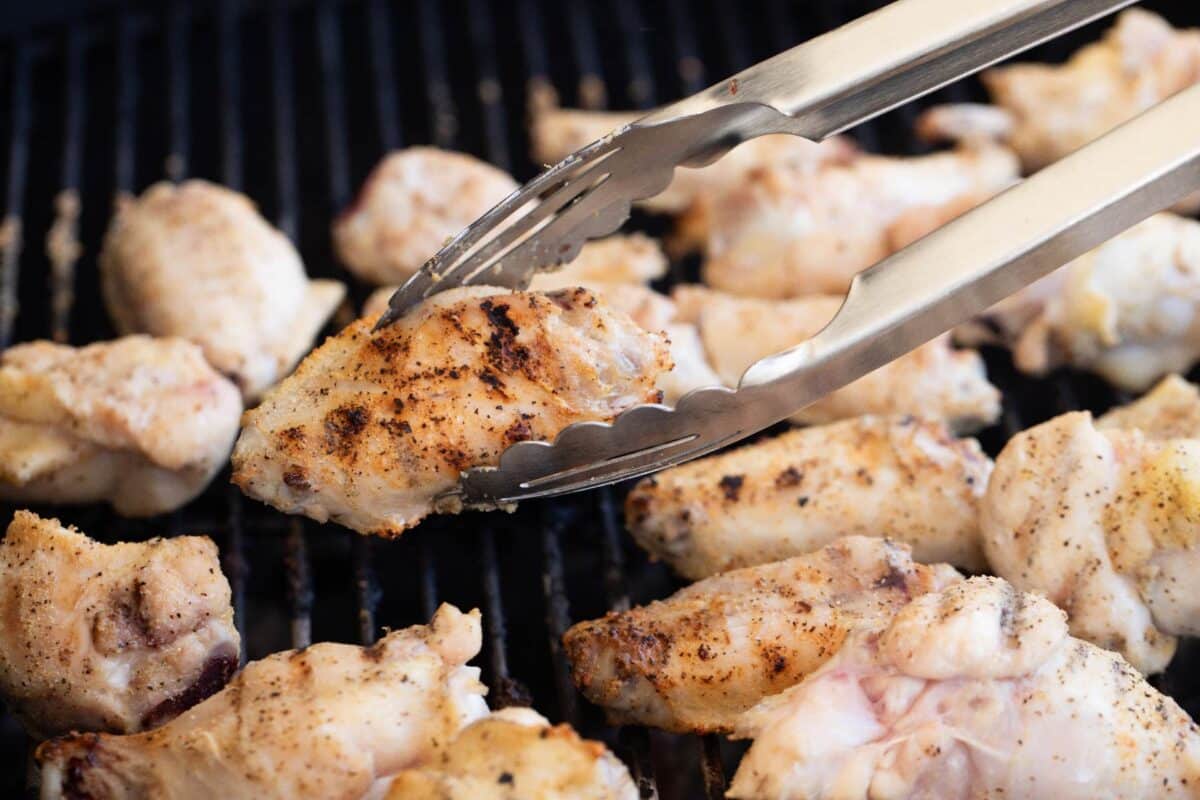 Tongs flipping wings on the grill.