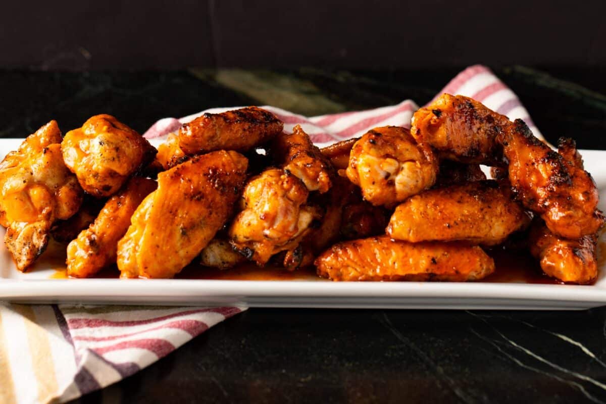 Hot wings on white platter, on top of striped tablecloth.