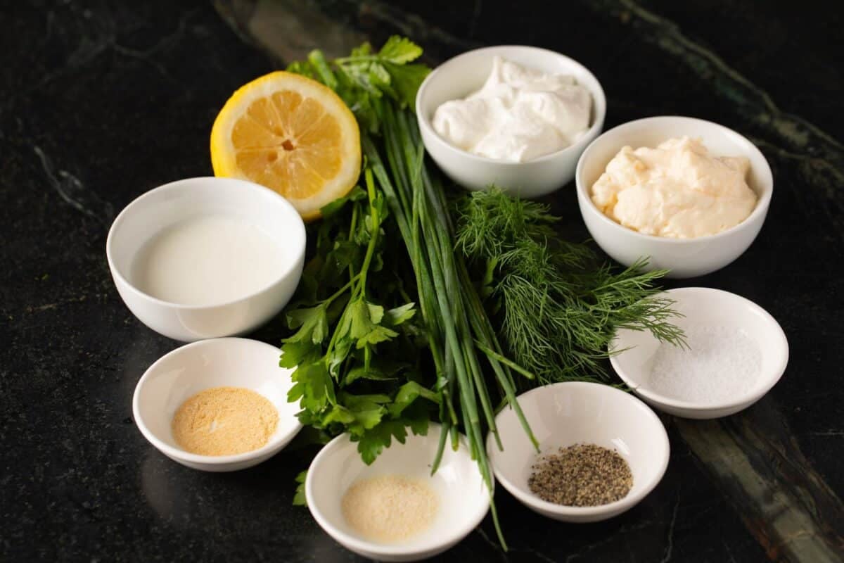 Fresh dill and white bowls of raw ingredients on black countertop.