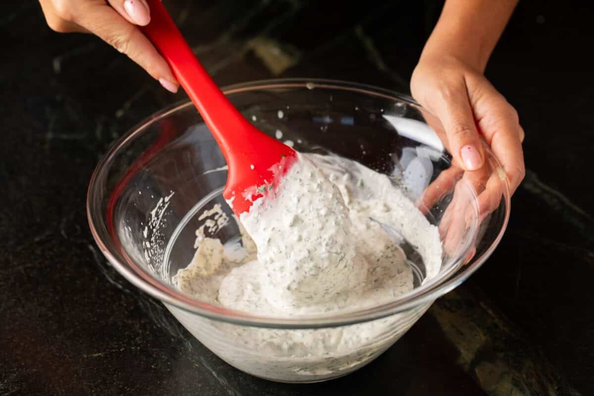 Rubber spatula mixing dressing in glass bowl.