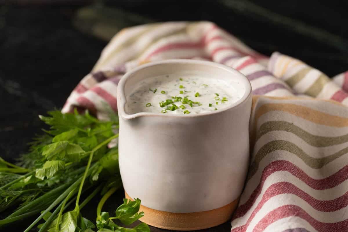 Ranch dressing in white jar next to cloth napkin and fresh dill.