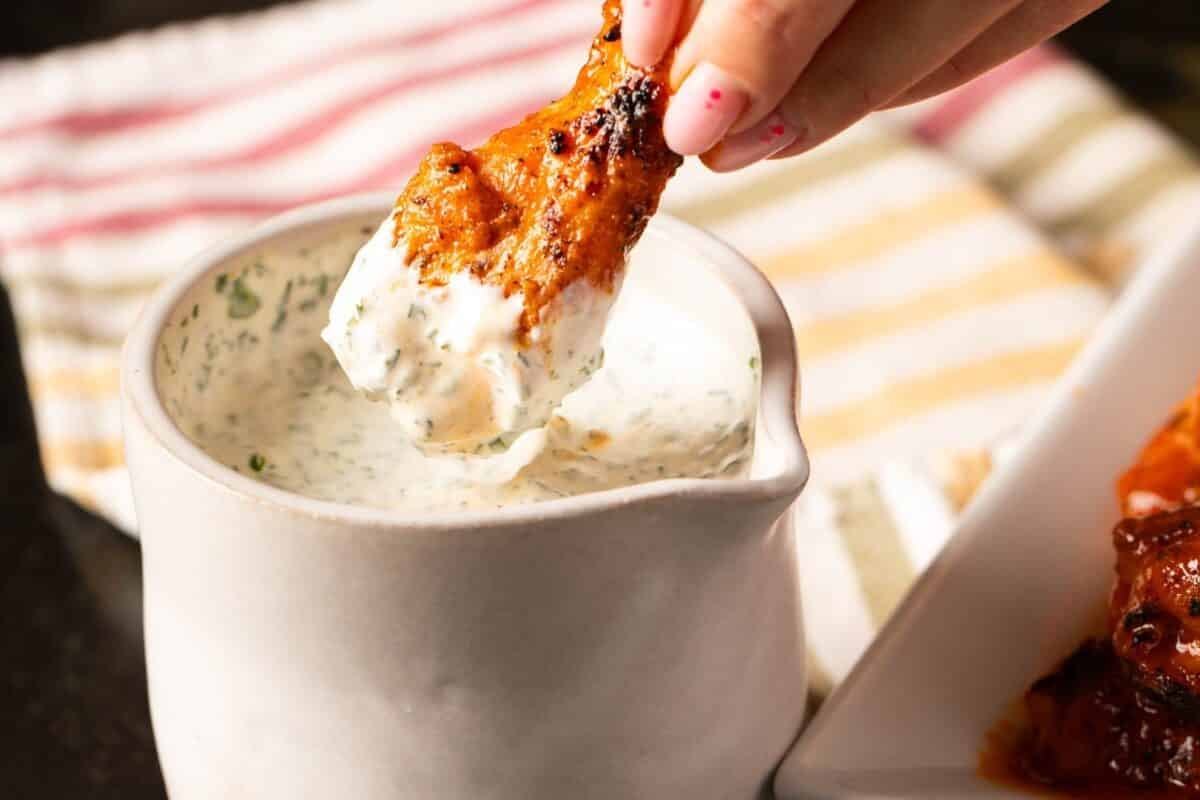 Buffalo wing being dipped into jar of dipping sauce.