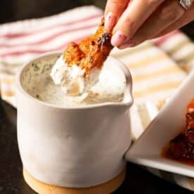 Buffalo wing being dipped into jar of dipping sauce.