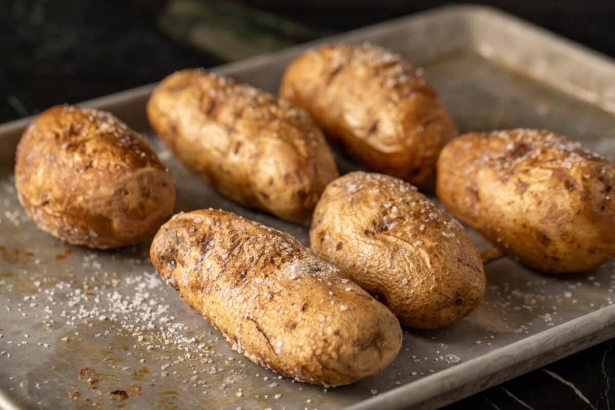 Baked potatoes seasoned with salt on metal baking sheet.