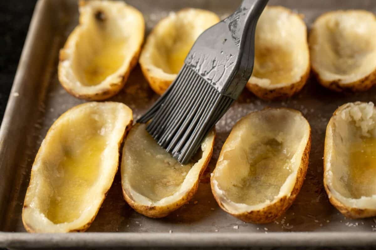 Hollowed potatoes on baking sheet being brushed with butter.