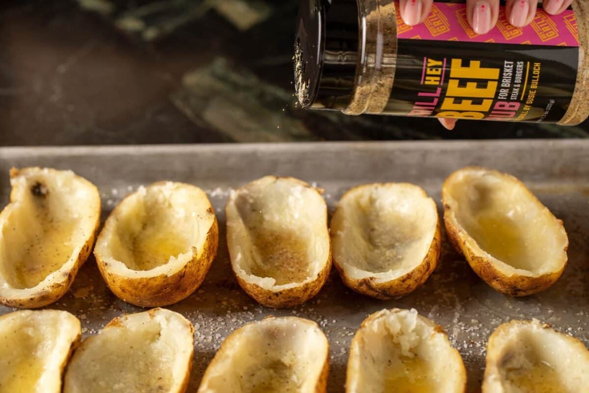 Hollowed potato skins on baking sheet being sprinkled with Beef Rub.