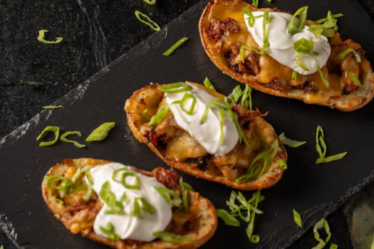 Potato skins on a black platter, loaded with pulled pork, sour cream, and cheese.