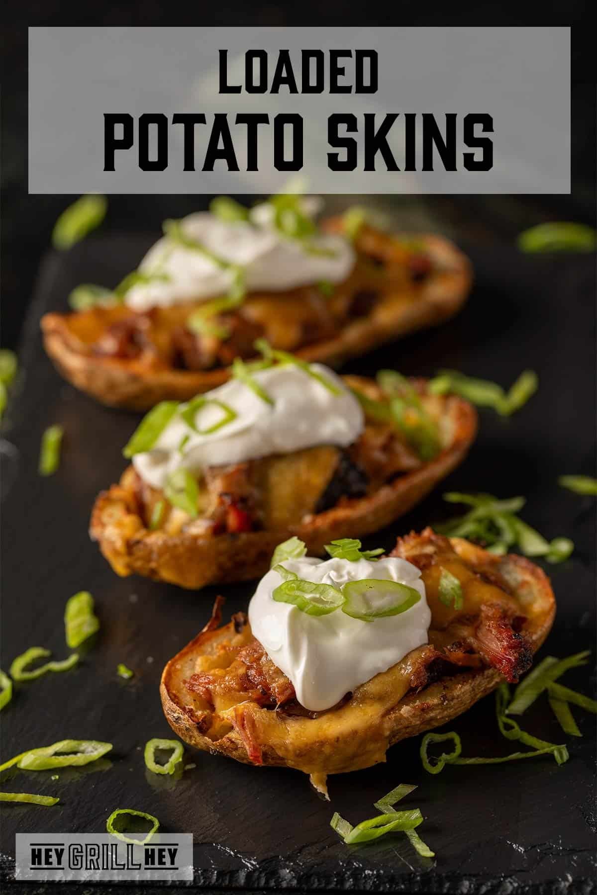 Potato skins with pulled pork, sour cream, and green onions on black platter. Text reads "Loaded Potato Skins."