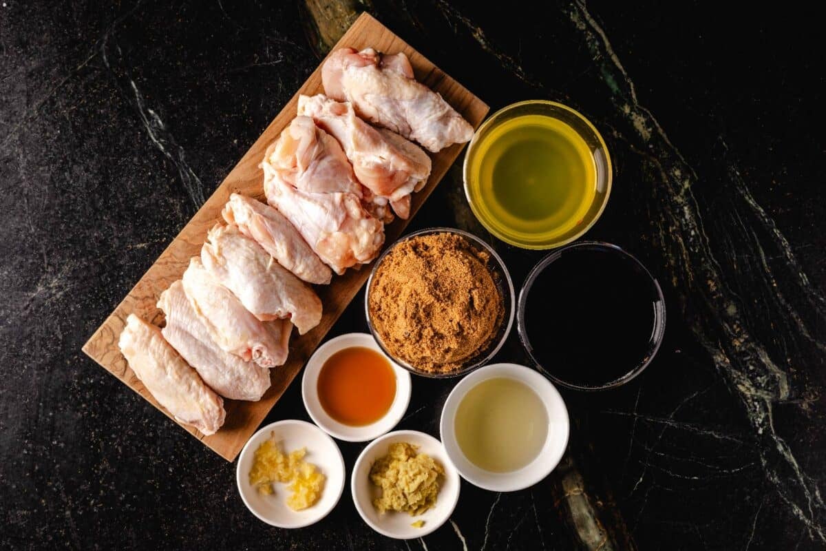 Marinade ingredients in glass bowls next to cutting board with raw chicken.