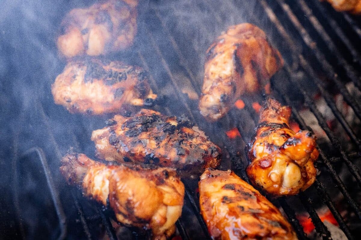 Chicken on grill grates in wafting smoke.