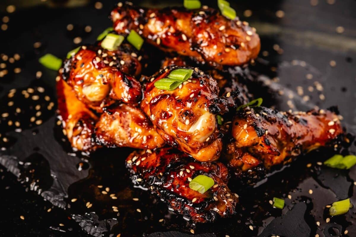 Teriyaki wings piled on a black serving platter, sprinkled with green onion slices.