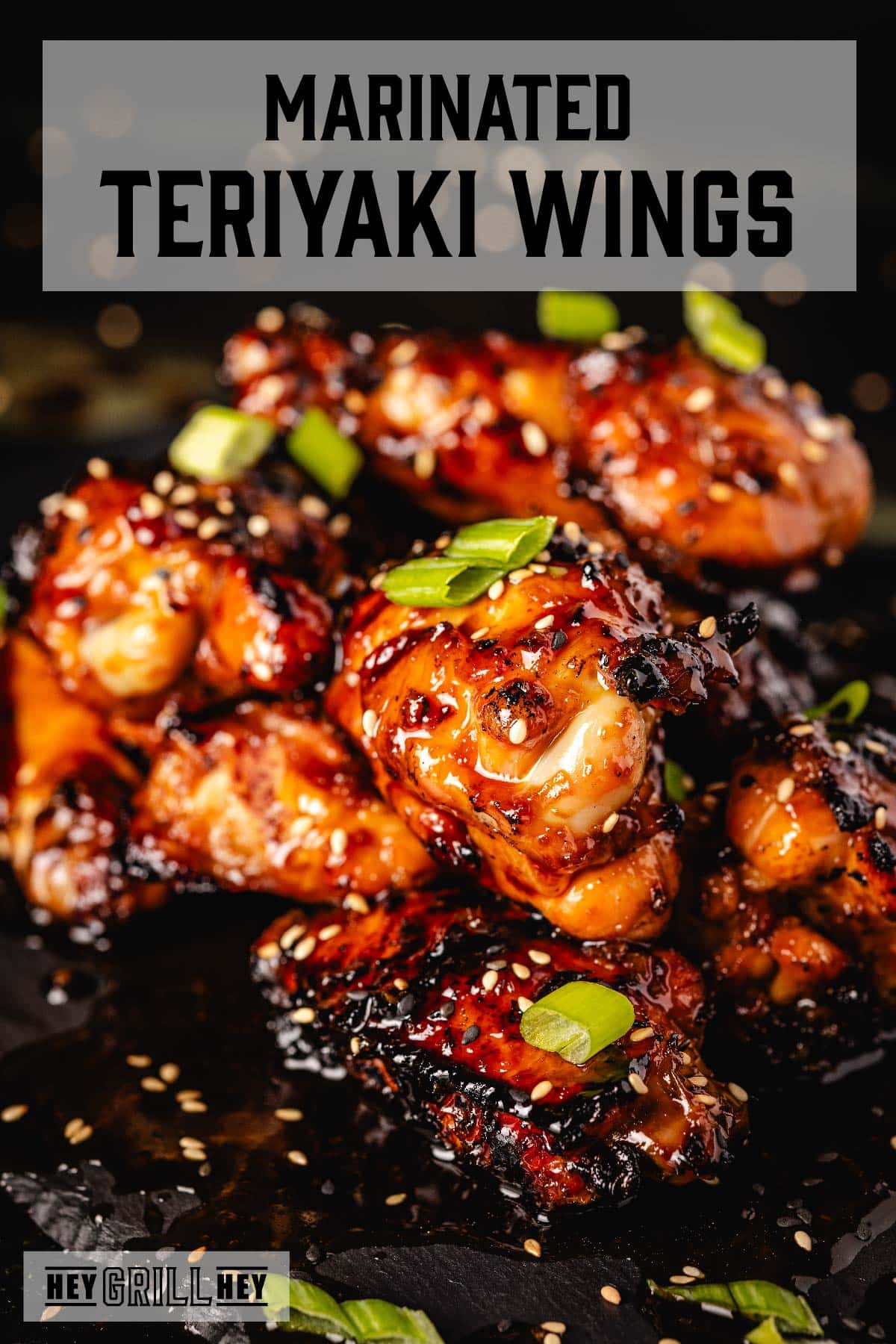 Chicken wings with green onion slices on a black platter. Text reads "Marinated Teriyaki Wings."