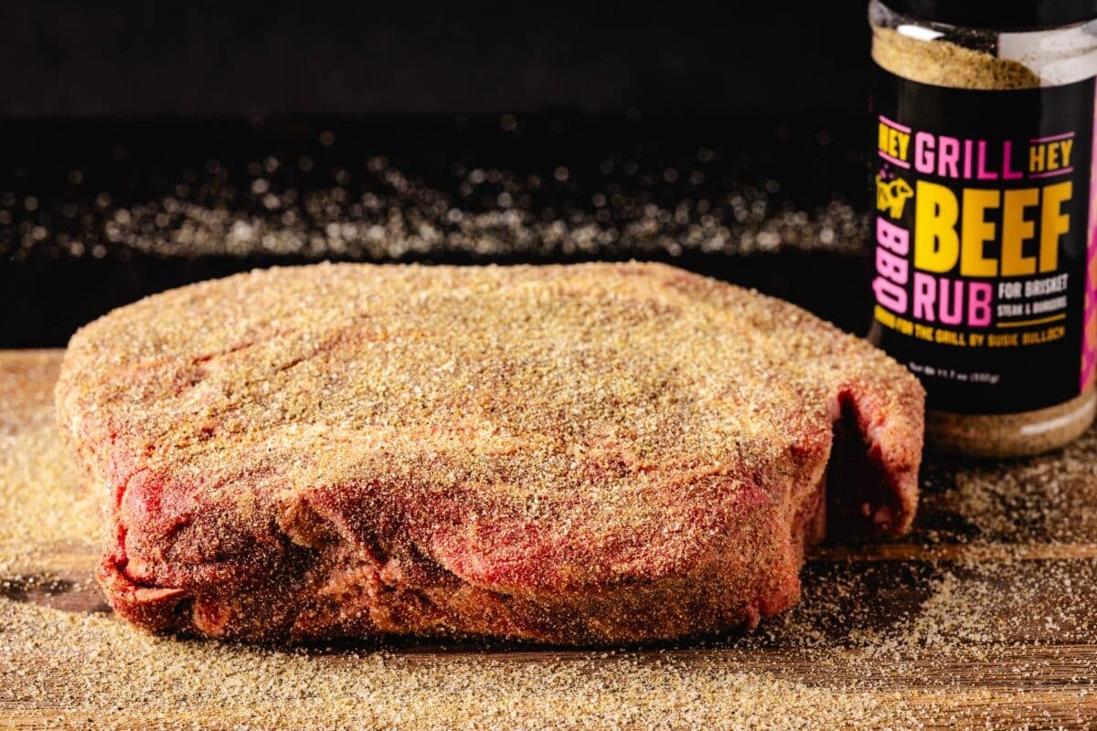 A seasoned beef cut on a cutting board next to a bottle of Beef Rub.