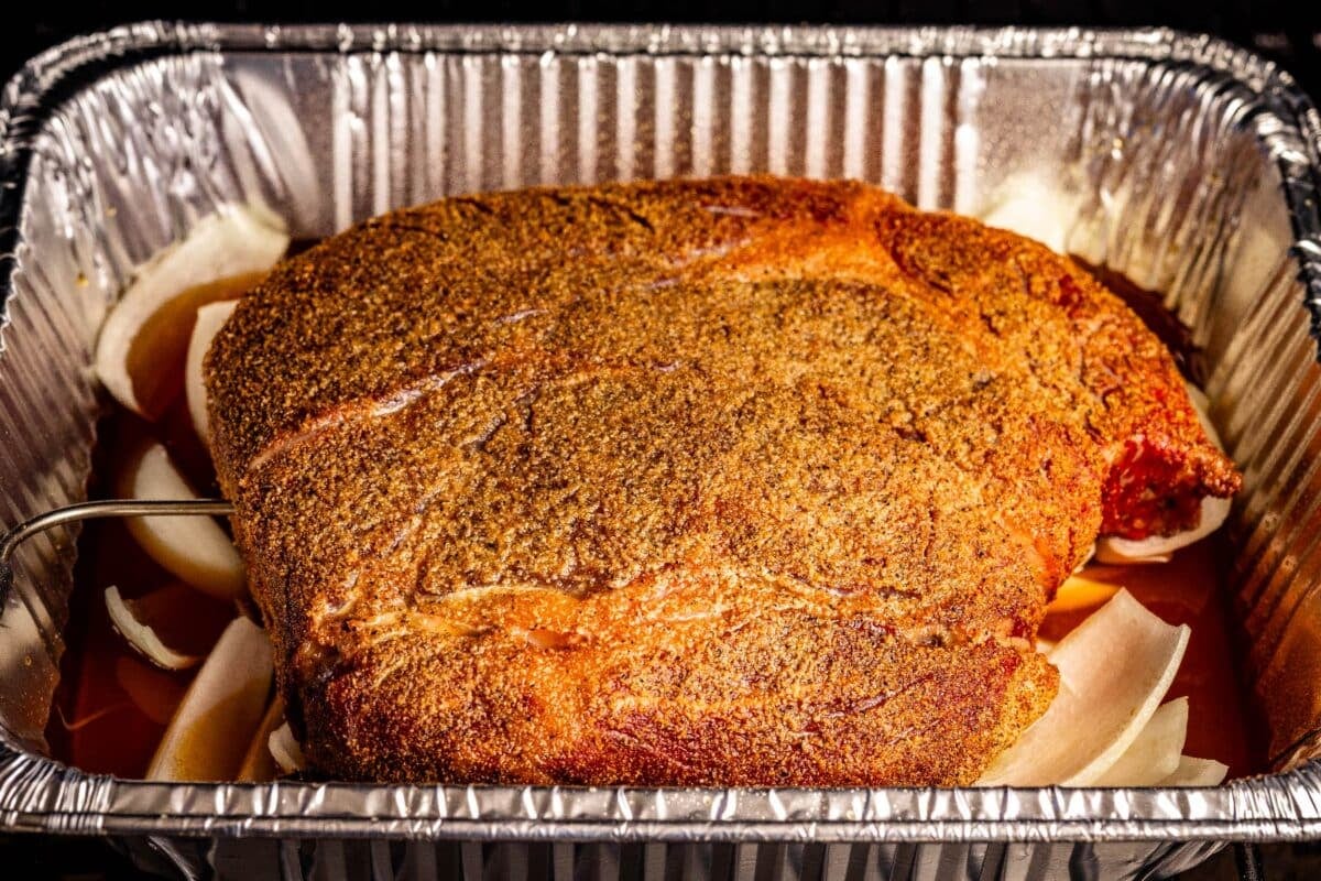 Beef roast in an aluminum pan with sliced onions and beef stock.