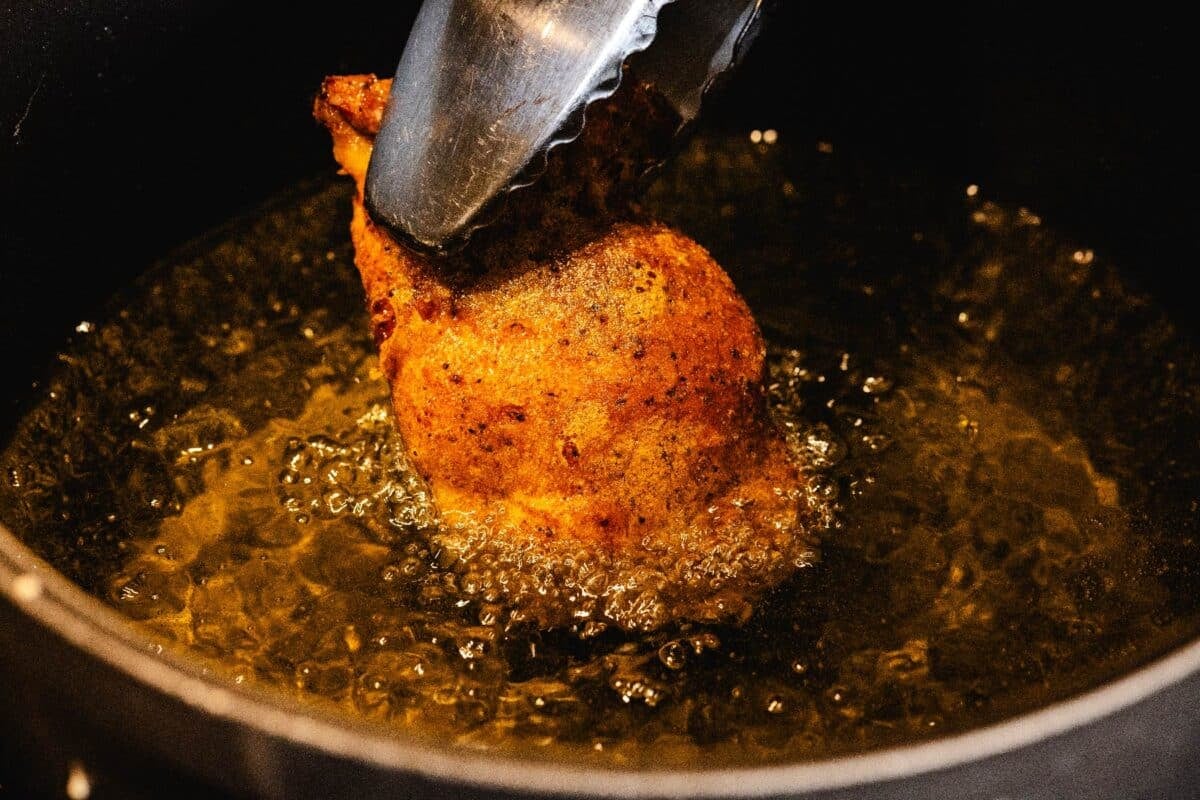 Breast frying in oil being flipped with tongs.