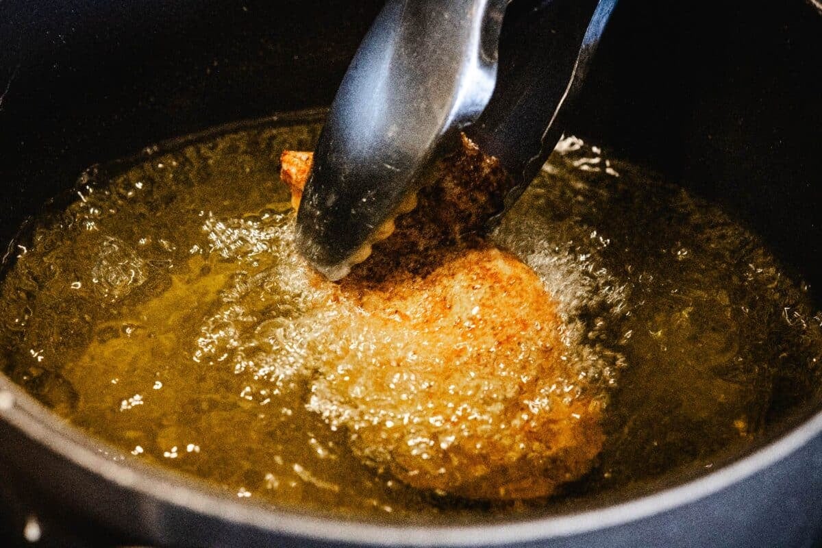 Tender being flipped with tongs in frying oil.