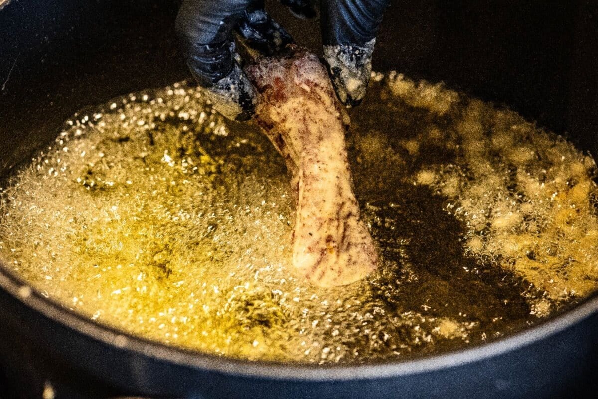 Rib being fried in oil in skillet.