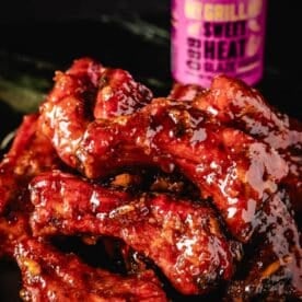 Glazed, smoked party ribs in front of glaze bottle.