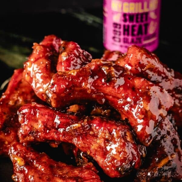 Glazed, smoked party ribs in front of glaze bottle.