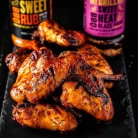 Smoked chicken wings piled in front of bottles of Sweet Rub and Sweet Heat BBQ Glaze.