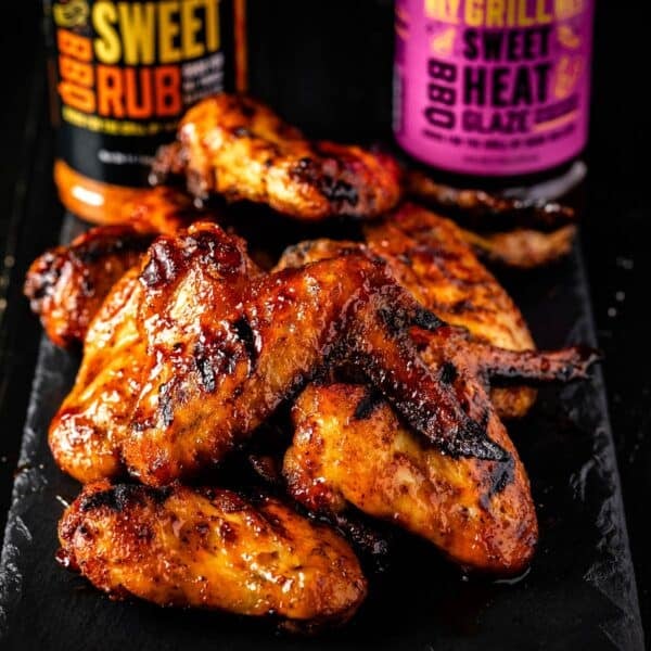 Smoked chicken wings piled in front of bottles of Sweet Rub and Sweet Heat BBQ Glaze.