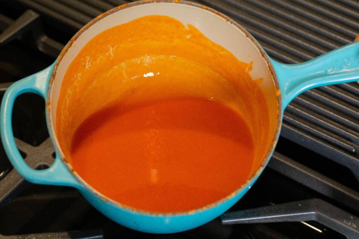 Buffalo sauce in a blue and white pot on a range.