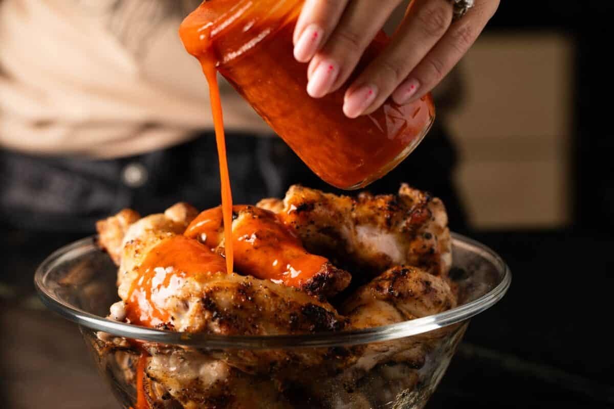 Grilled chicken wings in a glass bowl being sauced.