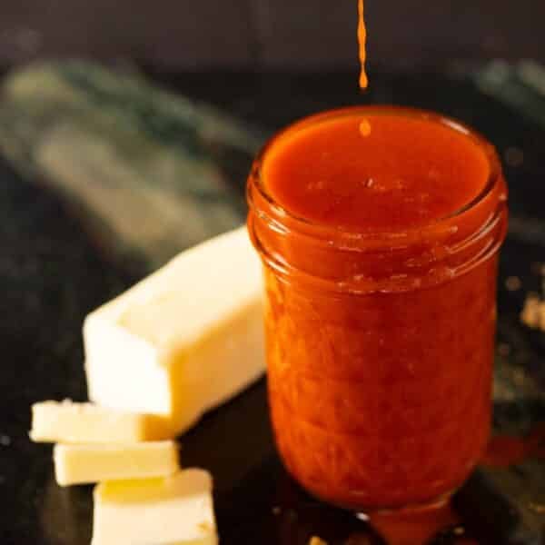 A clear mason jar with sauce, next to a stick of partially sliced butter.