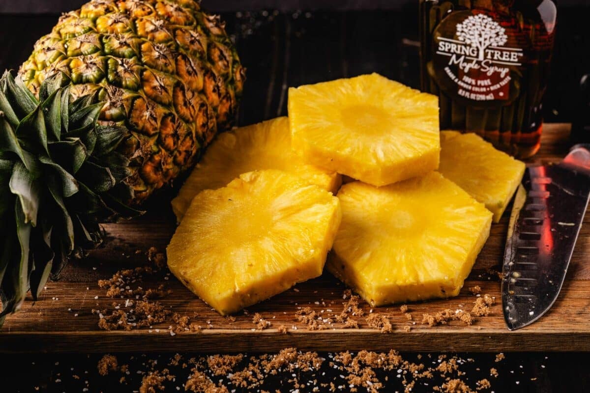 Whole and sliced pineapples on a cutting board with a knife.