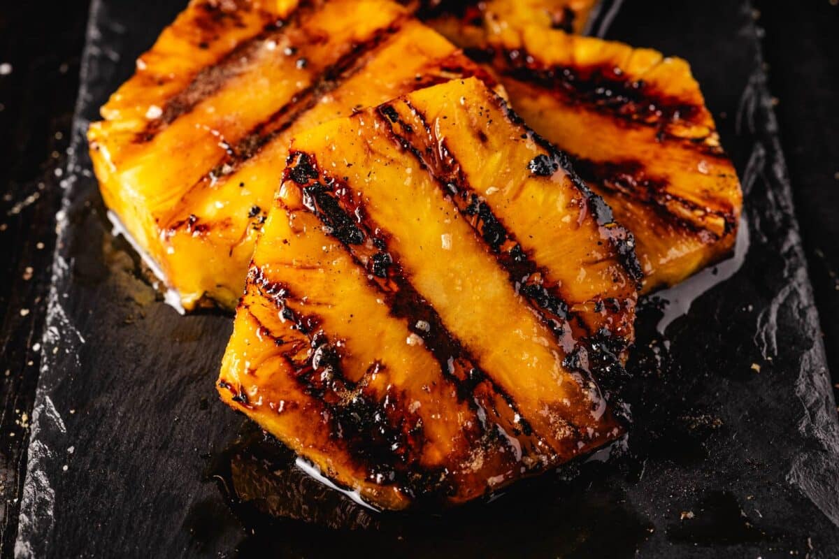 Grilled pineapple slices stacked on a black countertop.