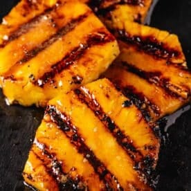 Grilled pineapple slices stacked on a black countertop.