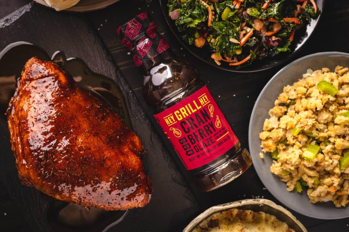 A bottle of sauce lying on a tabletop next to a bowl of corn, and a cooked turkey.