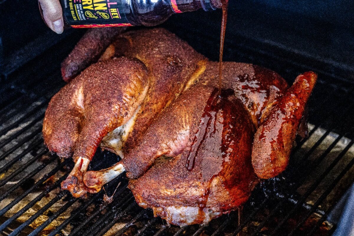 A turkey on the smoker being drizzled with cranberry glaze