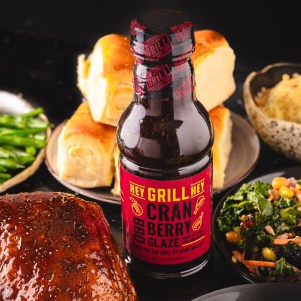 A bottle of Cranberry BBQ Glaze next to a smoked turkey and side dishes.