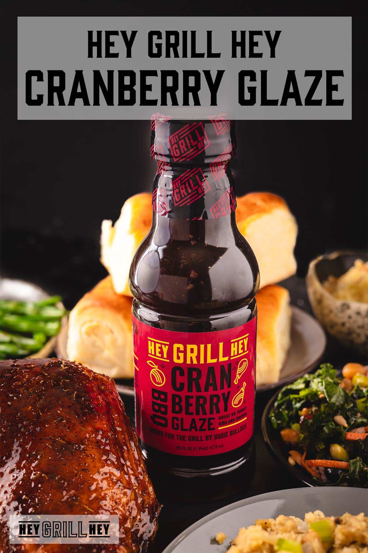 A bottle of BBQ glaze next to a smoked turkey and various side dishes. The text overlay reads "Hey Grill Hey Cranberry Glaze."