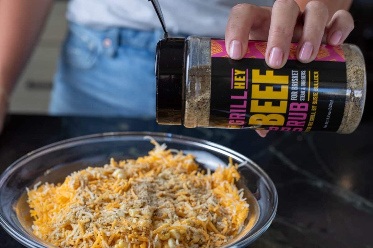 Beef seasoning being sprinkled on dry ingredients in a glass bowl.