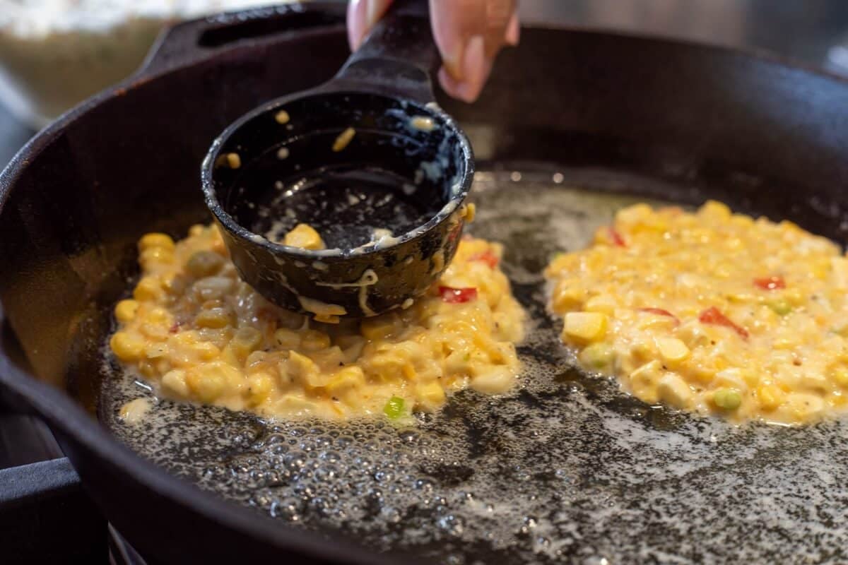 Measuring cup smashing batter scoop in a cast iron skillet.