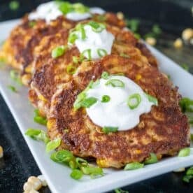 Corn fritters on a white plate, sprinkled with green onions and corn kernels.