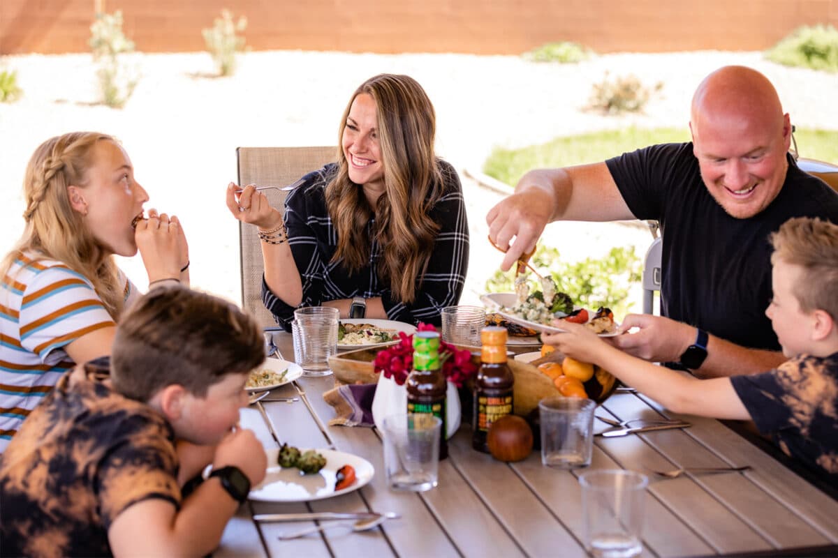 A family sitting around an outside table enjoying bbq together.