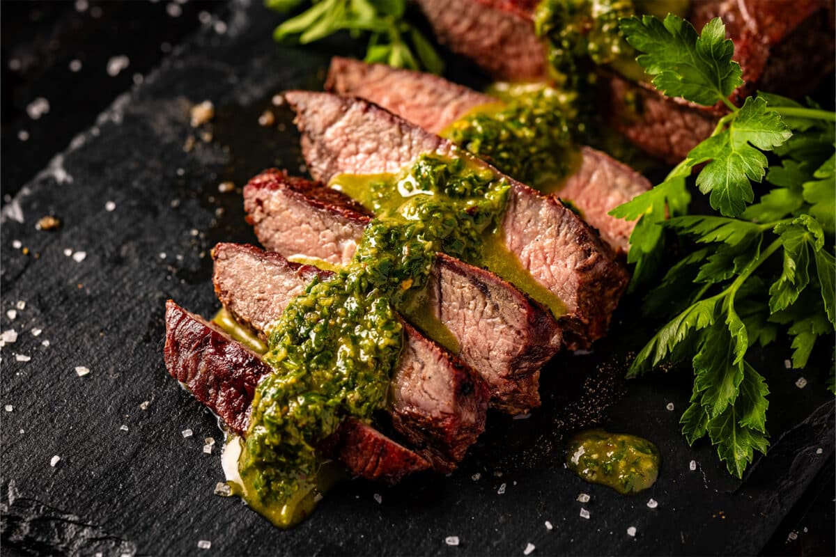 a flat iron steak cooked to medium rare, sliced into strips, and topped with Chimichurri on top of a black serving platter.