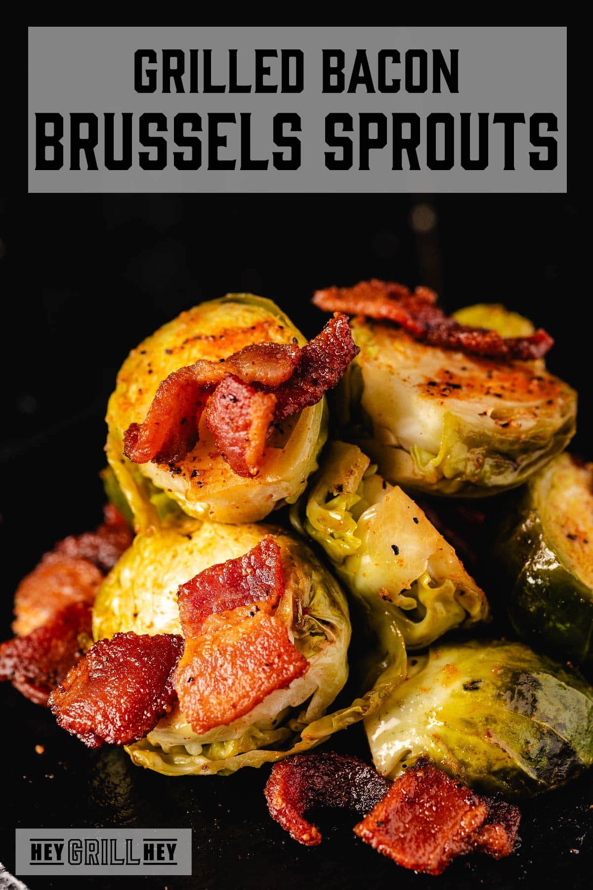 Sliced and grilled Brussels sprouts piled and topped with chopped bacon. The text overlay and the top reads "Grilled Bacon Brussels Sprouts," and the small one at the bottom reads "Hey Grill Hey."