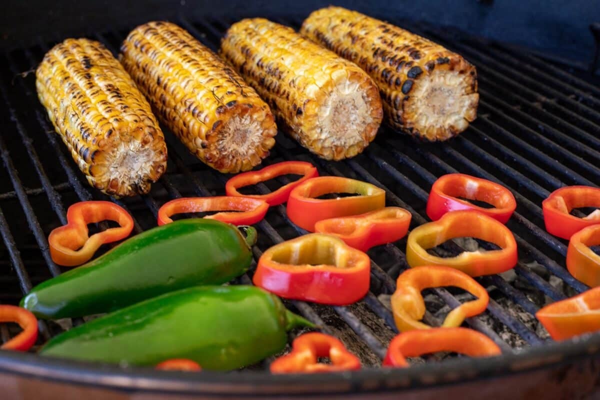 Earns of corn and sliced peppers on grill grates.