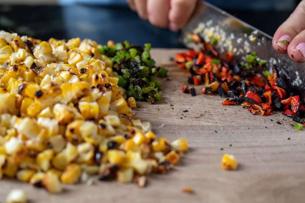 A knife slicing red peppers on a cutting board next to other chopped veggies.