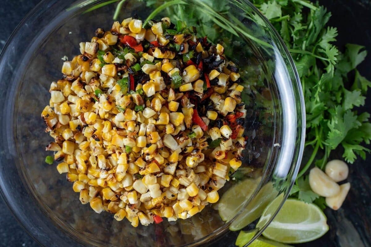 Chopped veggies in a glass bowl next to lime wedges, cilantro, and garlic bulbs.