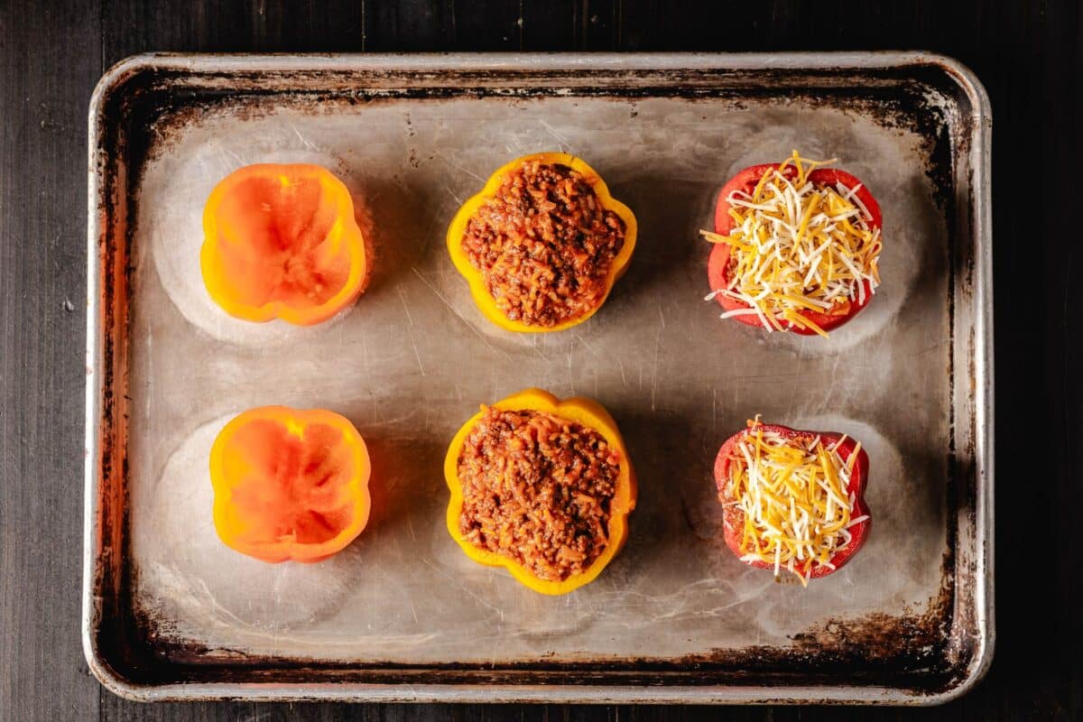 A baking sheet with six bell pepper halves with filling.