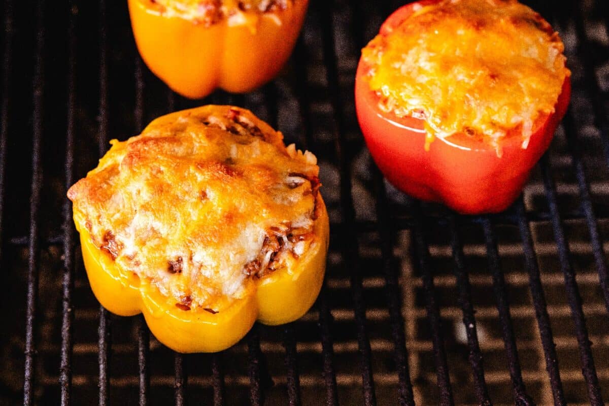 Filled peppers topped with cheese, sitting on grill grates.